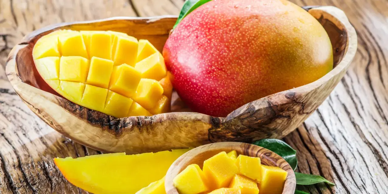 Soczyste, pokrojone w kostkę i w całości mango w drewnianej misce. Owoc ten zawiera mnóstwo witamin.