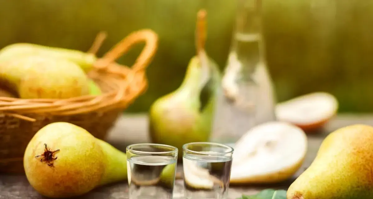 Frische Birnen und zwei Gläschen Schnaps auf Holztisch. Ein Korb voller Birnen im Hintergrund. Perfekt für ein Birnenschnaps Rezept.