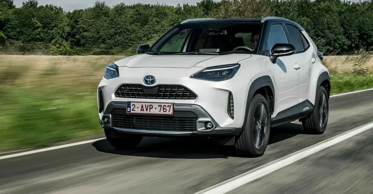 Biały Yaris Cross Hybrid jedzie po drodze, otoczony zielenią.