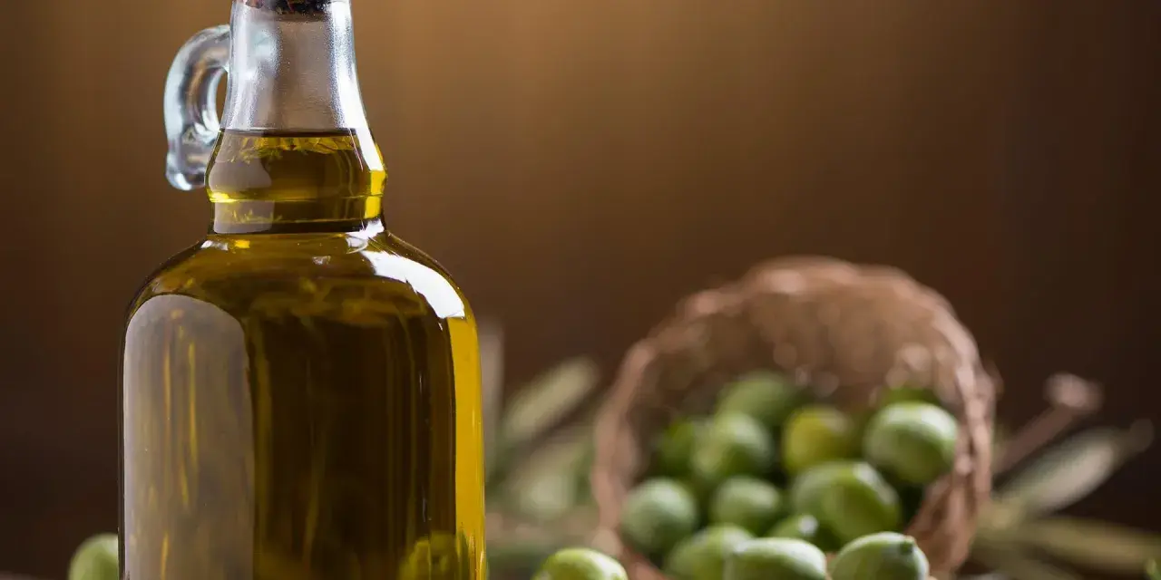 Bottiglia di olio extravergine d'oliva accanto a olive verdi, per capire la differenza tra olio di oliva e olio extravergine.