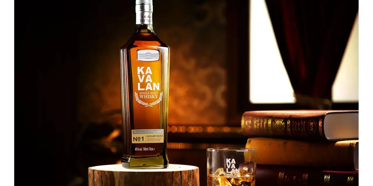 Butelka Kavalan Single Malt Whisky, uznawana za najlepszą polską whisky, obok szklanki z lodem i sterty książek.