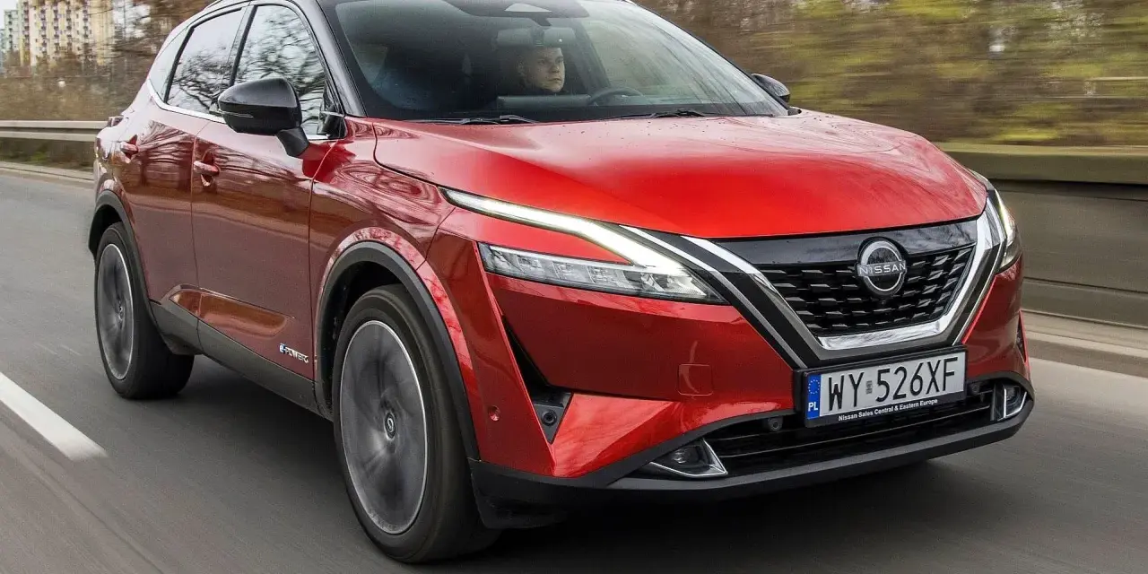 Czerwony Nissan Qashqai 2023 z napędem e-POWER jedzie po drodze, za kierownicą siedzi kierowca.