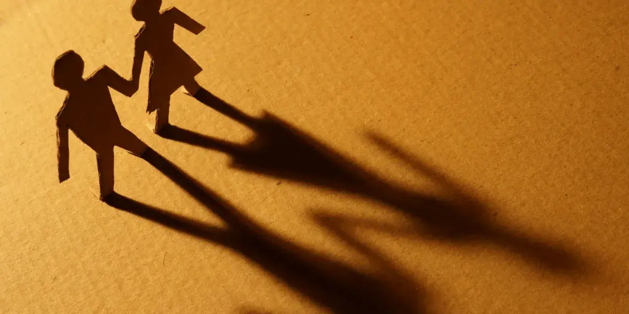 Zwei Papierfiguren, die sich an den Händen halten. Eine Figur scheint sich abzuwenden, während die andere bleibt. Sie sind noch verheiratet und eine neue Beziehung beginnt.