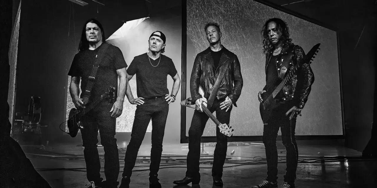James Hetfield und Metallica im Jahr 2000, bereit für die Bühne. Die Bandmitglieder stehen in dunkler Kleidung, einige mit Gitarren.