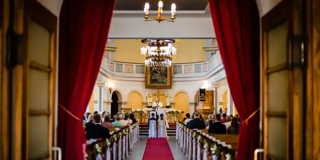 Ślub w kościele. Para młoda przed ołtarzem, ksiądz udziela im błogosławieństwa. Wszyscy zgromadzeni są chrześcijanami, a ten konkretny obrządek jest katolicki.