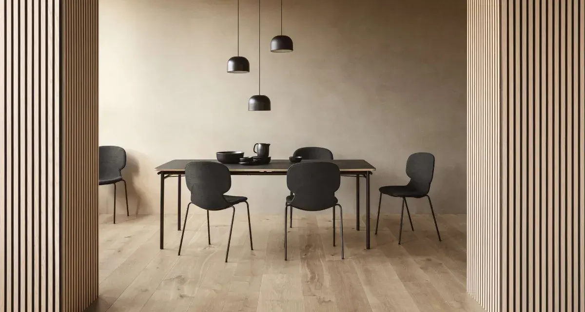 Jadalnia w stylu soft minimalism: czarne krzesła i stół na tle beżowej ściany, oświetlone lampami.