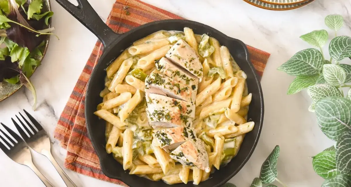 Deliciosa pasta con pollo en sartén, cubierta con hierbas frescas. Acompañada de una ensalada verde y tenedores.