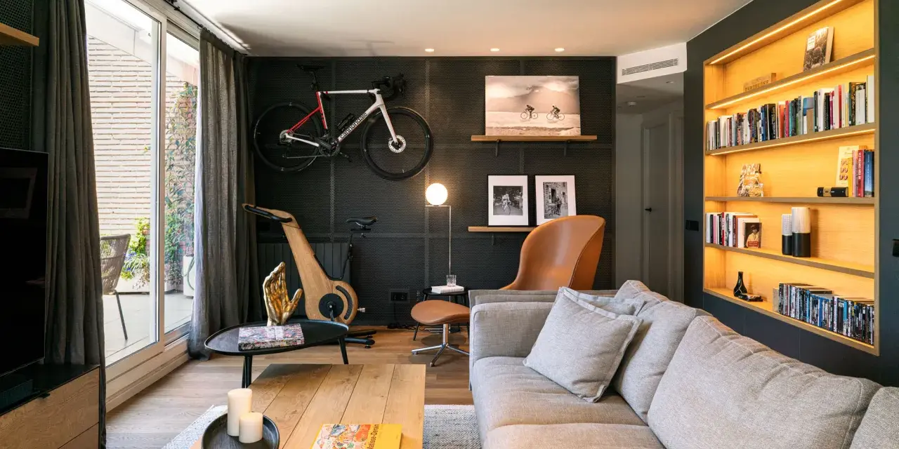 Un salón moderno con bicicleta de carretera colgada, máquina de ciclismo de madera y estanterías iluminadas. Inspiración decoración para deportistas.