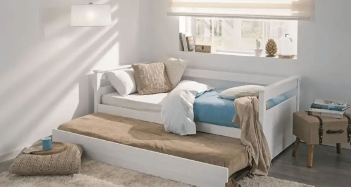 Cama nido blanca con colchones, cojines y manta en un dormitorio juvenil.