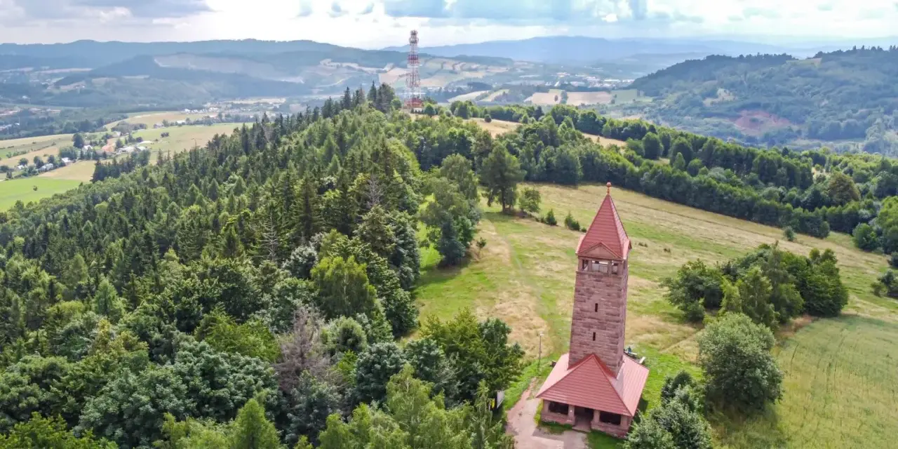 Wieża widokowa w górach zaprasza na podziwianie krajobrazu. W oddali widać maszt telekomunikacyjny.