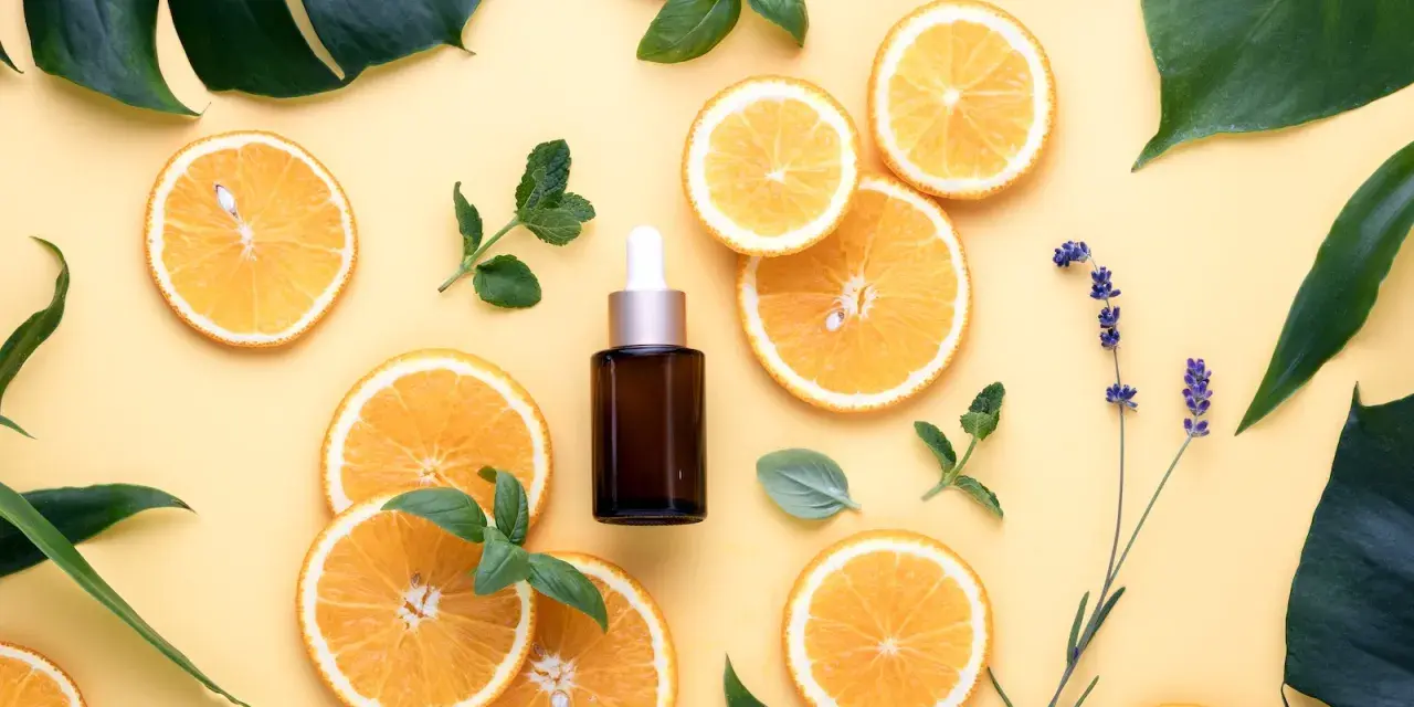 Siero viso con niacinamide e acido glicolico, circondato da fette d'arancia, foglie verdi e lavanda.