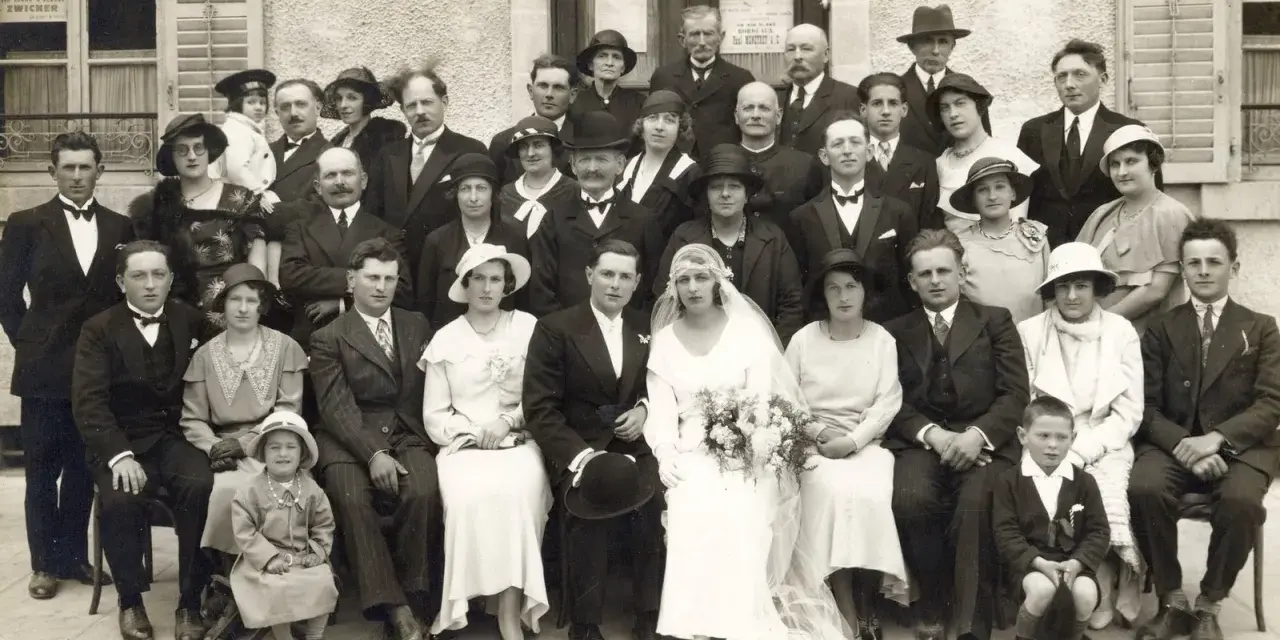 Un groupe pose pour une photo de mariage, peut-être pour un registre mariage. La mariée porte une robe blanche et un voile.