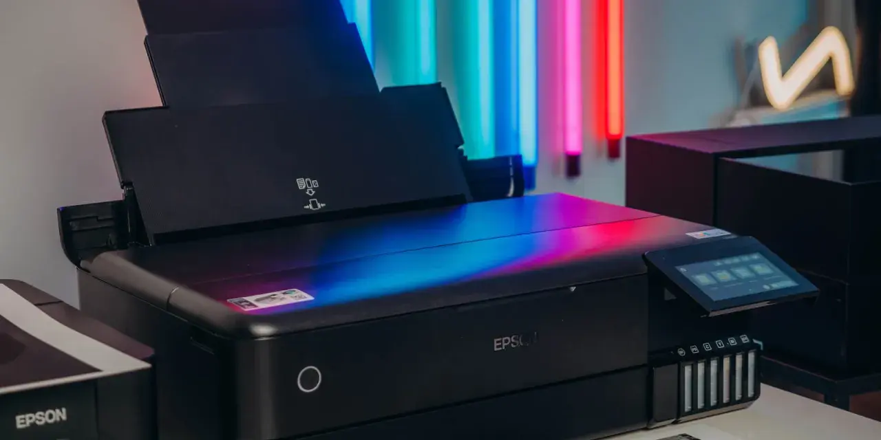 Czarna drukarka Epson z kolorowym ekranem, idealna do drukowania zdjęć. Obok stoi starszy model.