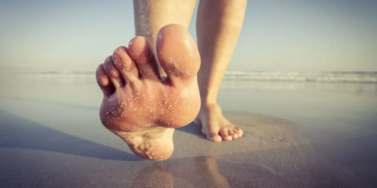 Paluch biegacza pokryty piaskiem, stopy na mokrym piasku przy plaży.
