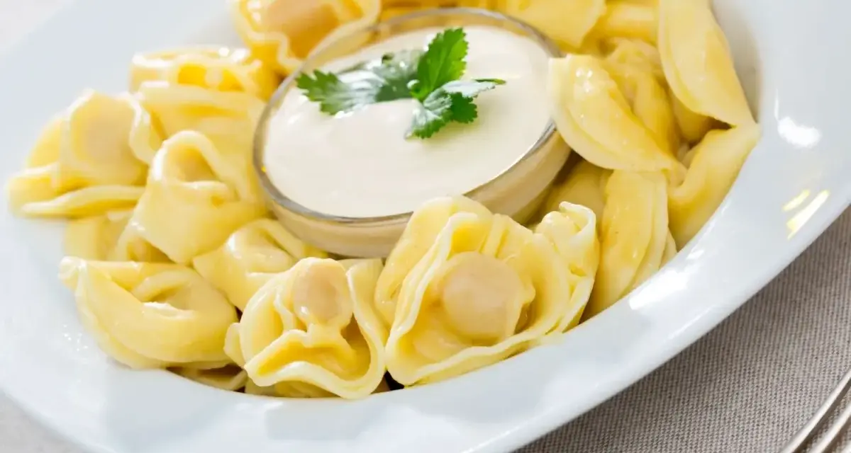 Pyszne pierożki tortellini w sosie śmietanowym, udekorowane natką pietruszki. Idealne danie na szybki obiad.