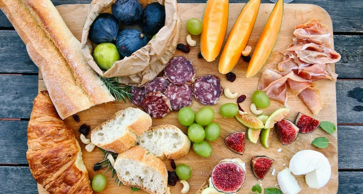 Tabla de quesos y embutidos: baguettes, croissants, higos, uvas, melón, jamón serrano y salami. Un festín que muestra qué comen los franceses.