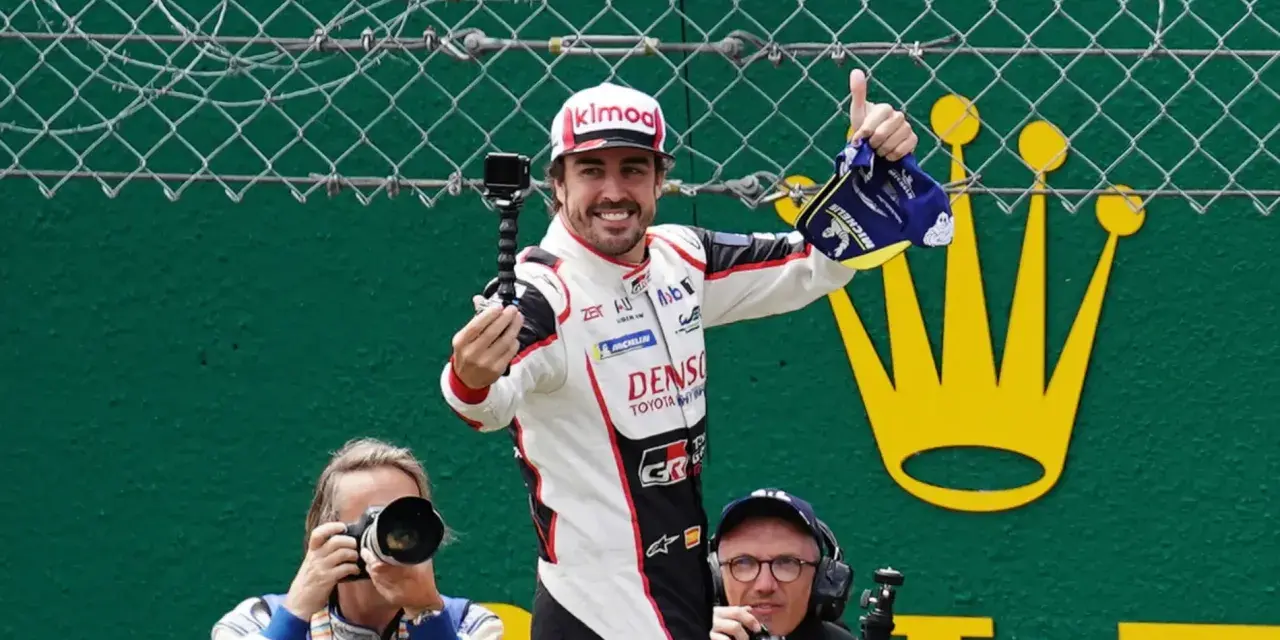 Fernando Alonso celebra su victoria en Le Mans, con una gorra y un trofeo. Fotógrafos capturan el momento.