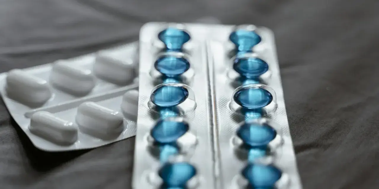 Dwa blistry leków: jeden z białymi kapsułkami, drugi z niebieskimi, które mogą być pregabalin sandoz.