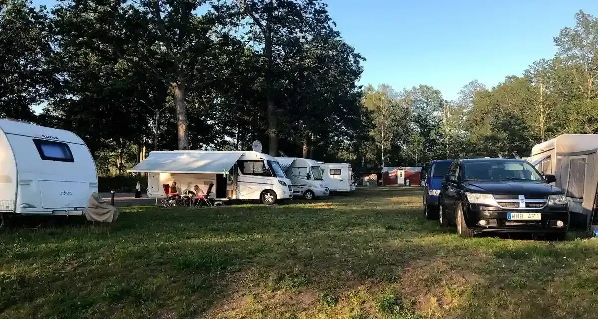 Solig dag på Alsterbro camping med husvagnar, husbilar och bilar uppställda på gräset.