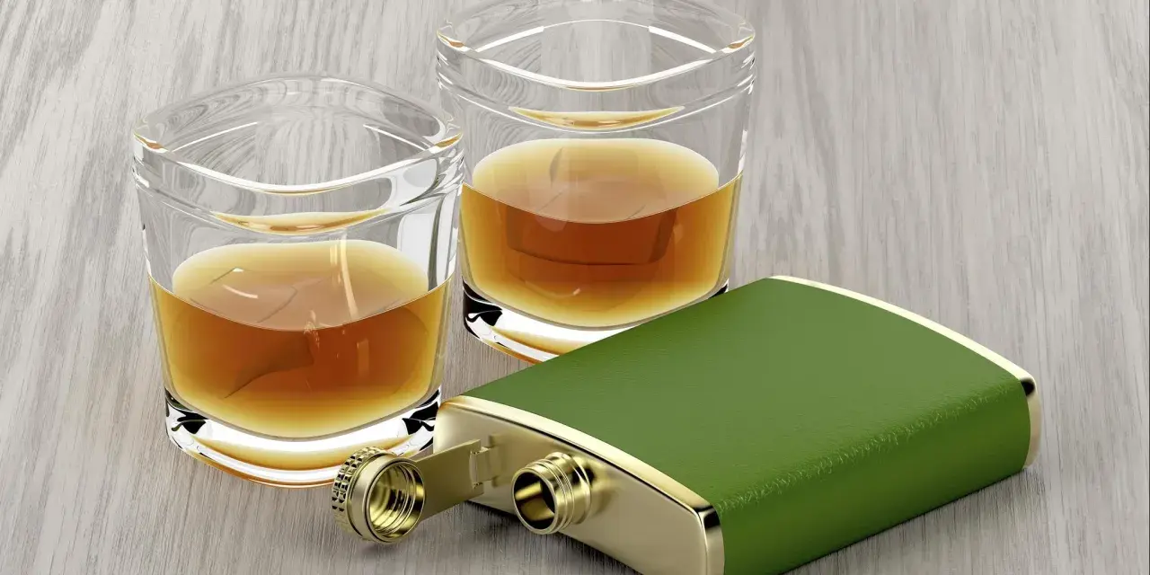 Zwei Gläser mit bernsteinfarbenem Whiskey und ein grüner Taschenflachmann. Ein 4 cl Whiskey hat ca. 90 Kalorien.