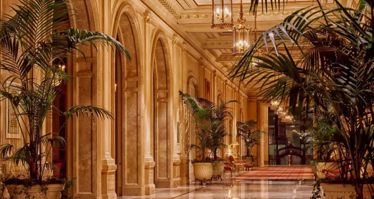 Elegancki korytarz z łukami i palmami, przypominający wnętrze najdroższego hotelu na świecie.
