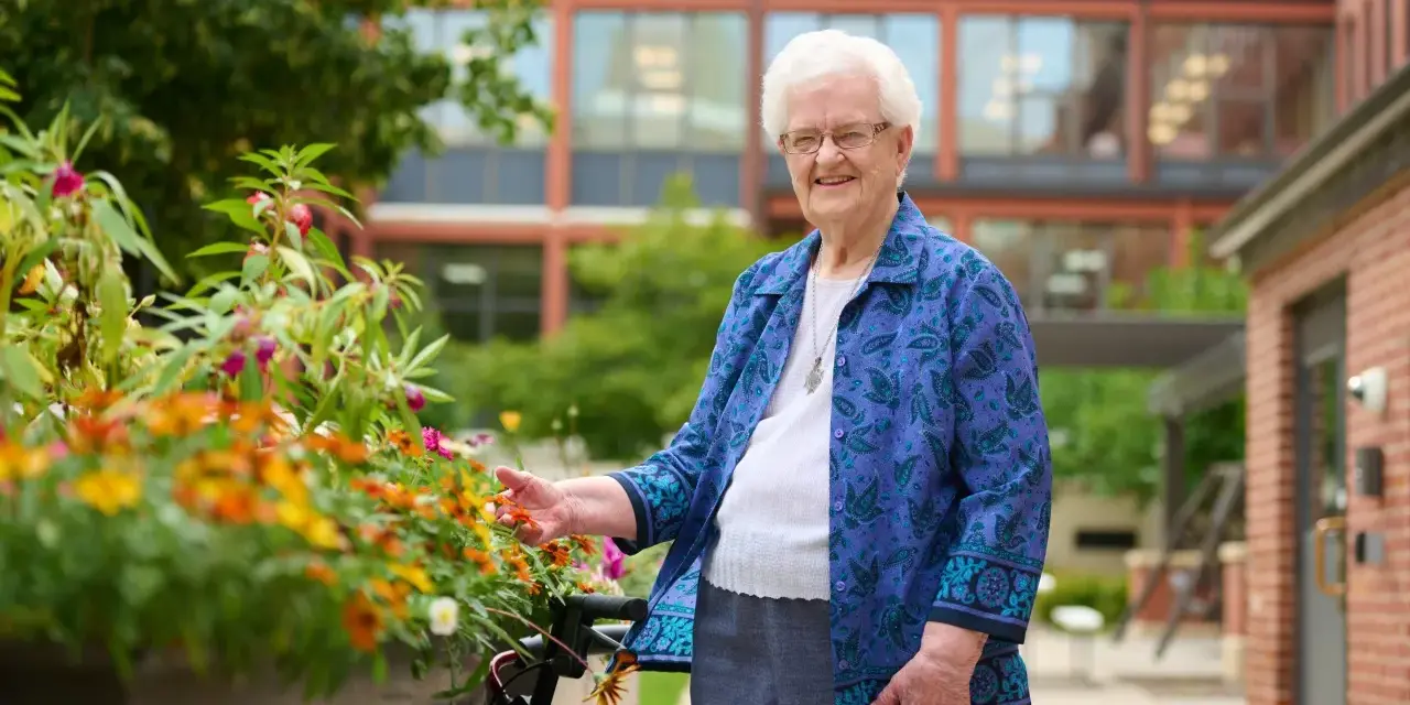 An elderly woman smiles, tending to flowers outside the St. Rose of Viterbo Convent.