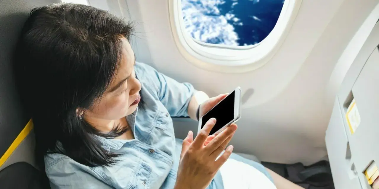 Kobieta z telefonem siedzi przy oknie w samolocie Ryanair, podziwiając chmury.