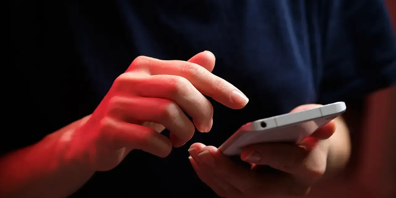 Dłonie z czerwonym podświetleniem obsługują smartfon, być może ustawiając **direct debit** na rachunki.
