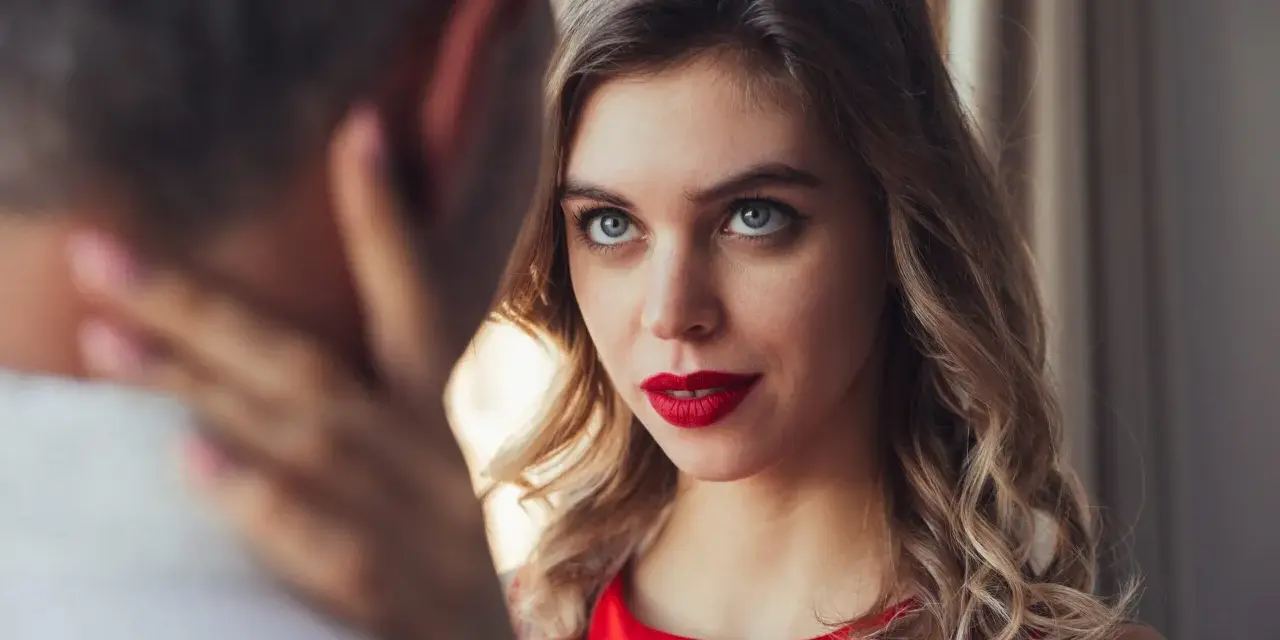 Un homme regarde intensément une femme aux yeux bleus et aux lèvres rouges, vêtue d'une robe rouge.