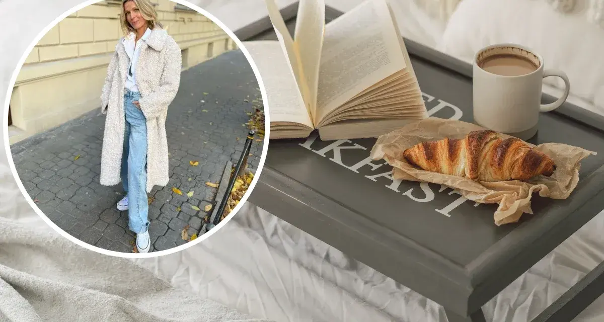 Kobieta w płaszczu z owczej wełny, symbolizującym quiet luxury, cieszy się śniadaniem w łóżku: książka, croissant i kawa.