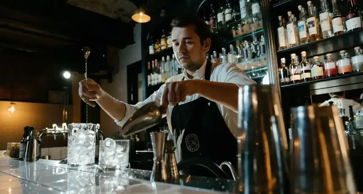 Barman przygotowuje drinki, pokazując, jak założyć drink bar. Na półkach stoją butelki alkoholi.