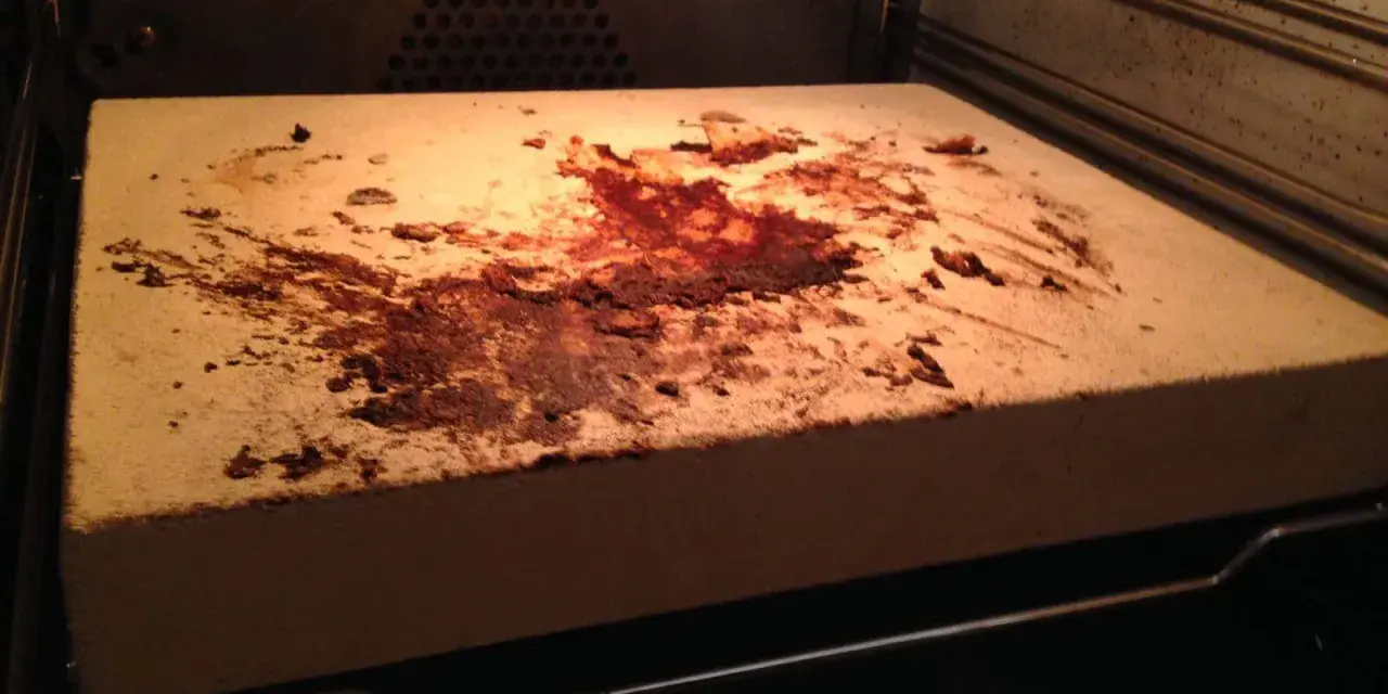 Ein schmutziger pizzastein mit braunen Flecken und Essensresten, der im Ofen liegt.