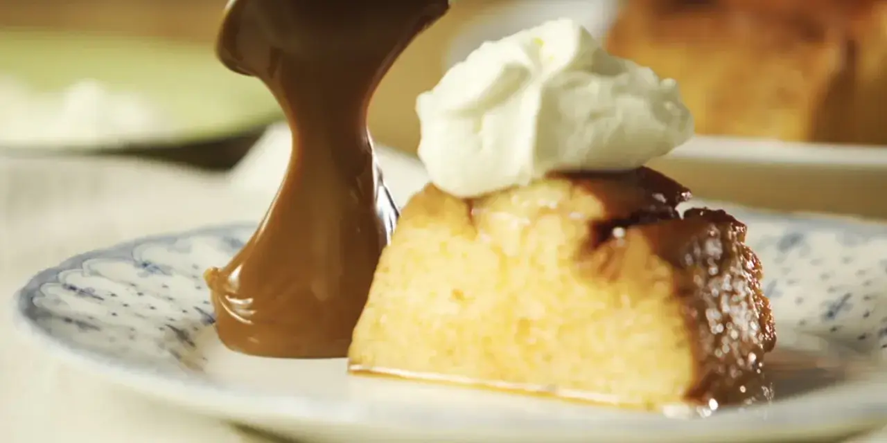 Un trozo de flan de 12 huevos, cubierto con caramelo y crema batida, servido en un plato con diseño azul.