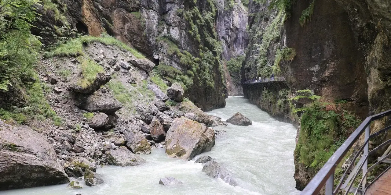 Aare Gorge, with its powerful river and dramatic cliffs, leads towards the Reichenbach Falls. A wooden walkway hugs the canyon wall.