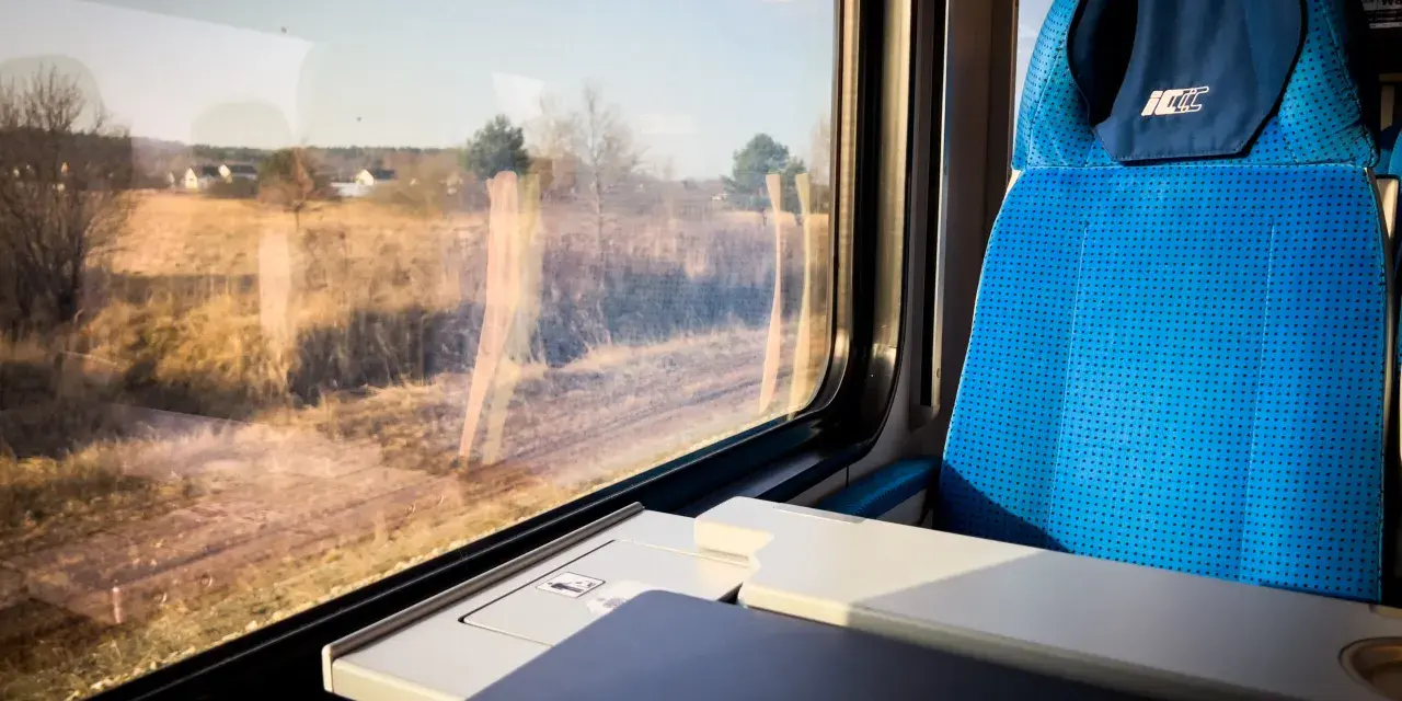 Podróż pociągiem z Katowic do Krakowa Balic. Widok z okna na krajobraz, obok niebieskie siedzenie i stolik z laptopem.