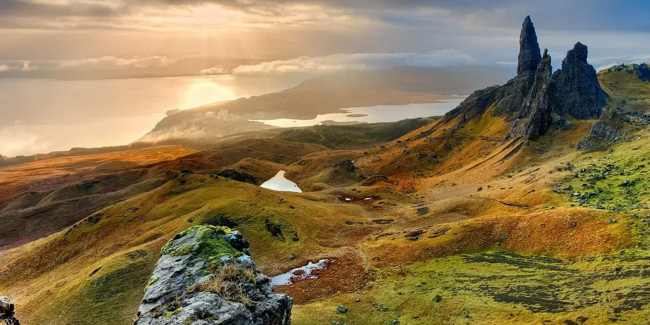Paysage écossais spectaculaire, photo HDR. Des collines ondulantes aux teintes dorées et vertes, des lacs scintillants et des formations rocheuses imposantes sous un ciel dramatique.
