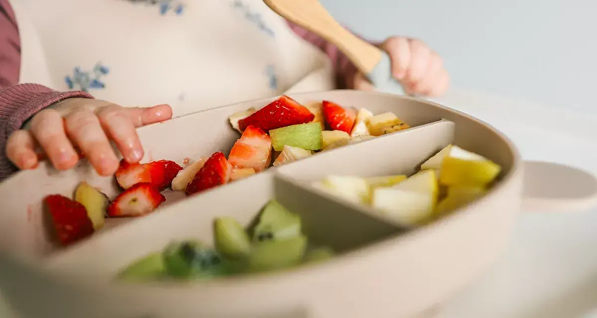 Bebé explorando fresas, kiwi y plátano en su plato. Es un buen momento para ofrecer fruta a los bebés.