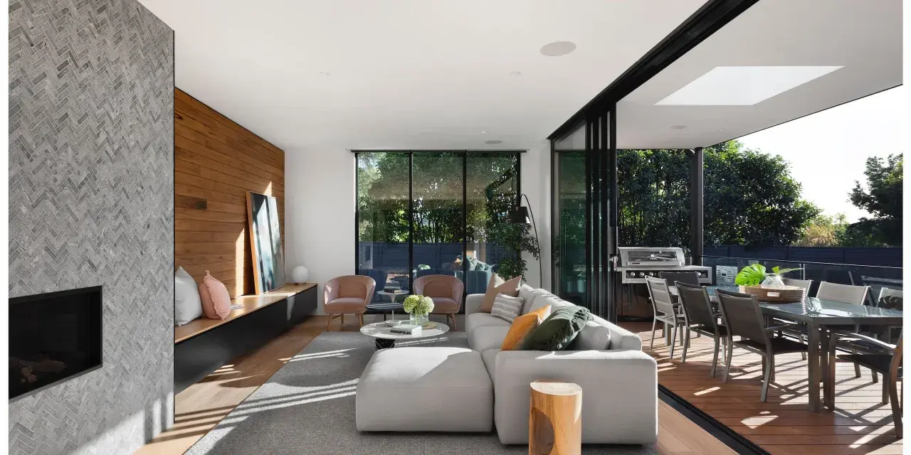 Elegante salón con chimenea de piedra, pared de madera y grandes ventanales que conectan con una terraza. Un ejemplo de las últimas tendencias interiorismo.
