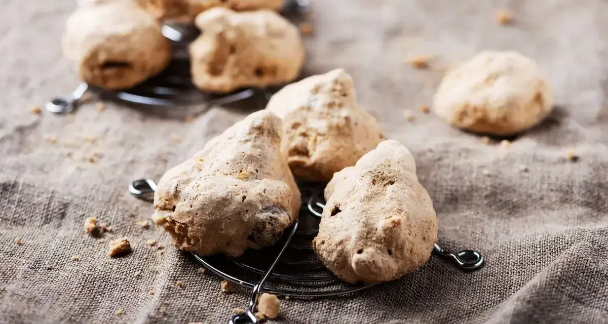 Biscotti meringati, dall'aspetto rustico, brutti ma buoni, su una griglia metallica e un telo grezzo.