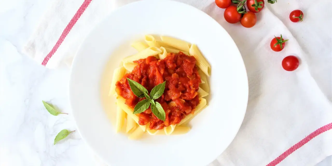 Penne z sosem pomidorowym i bazylią, obok świeże pomidorki koktajlowe.