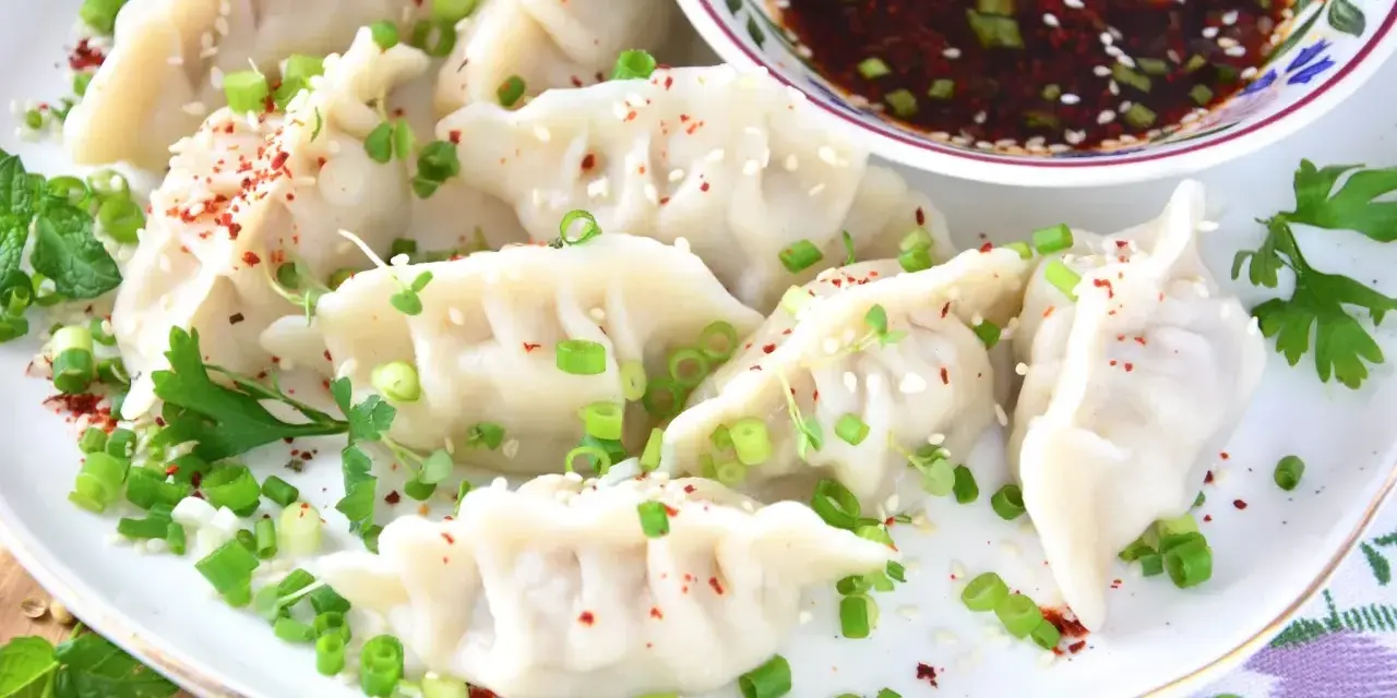 Pyszne pierożki gyoza, posypane szczypiorkiem i sezamem, gotowe do podania z sosem. Idealny przepis na domowe gyoza!