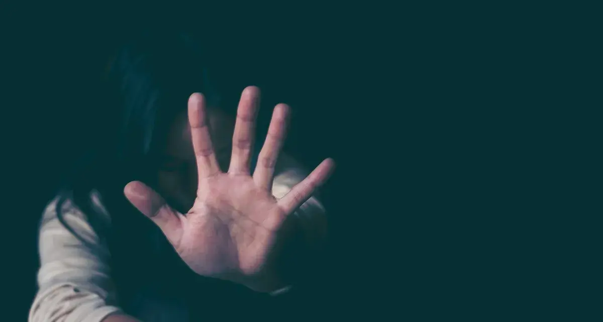 Frau hält Hand vor Gesicht, um sich vor psychischer Gewalt zu schützen. Sie fühlt sich bedroht, vielleicht wegen einer Wohnungszuweisung.
