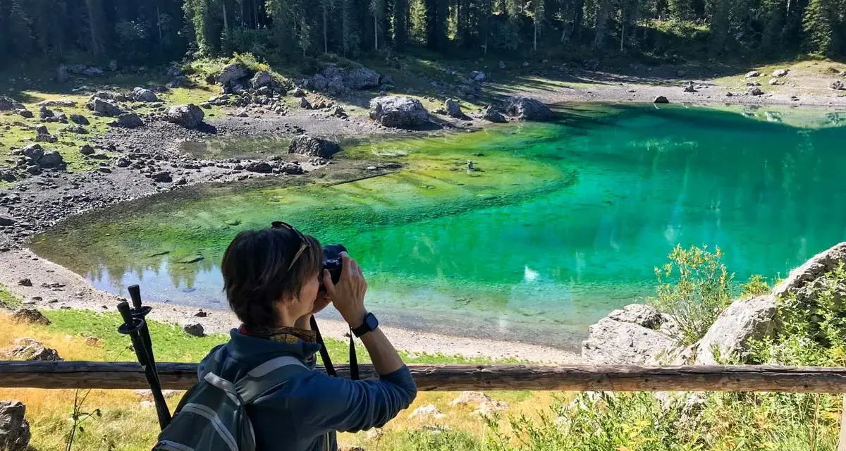 Donna con zaino e macchina fotografica cattura la bellezza del lago di Carezza, in Trentino Alto Adige.