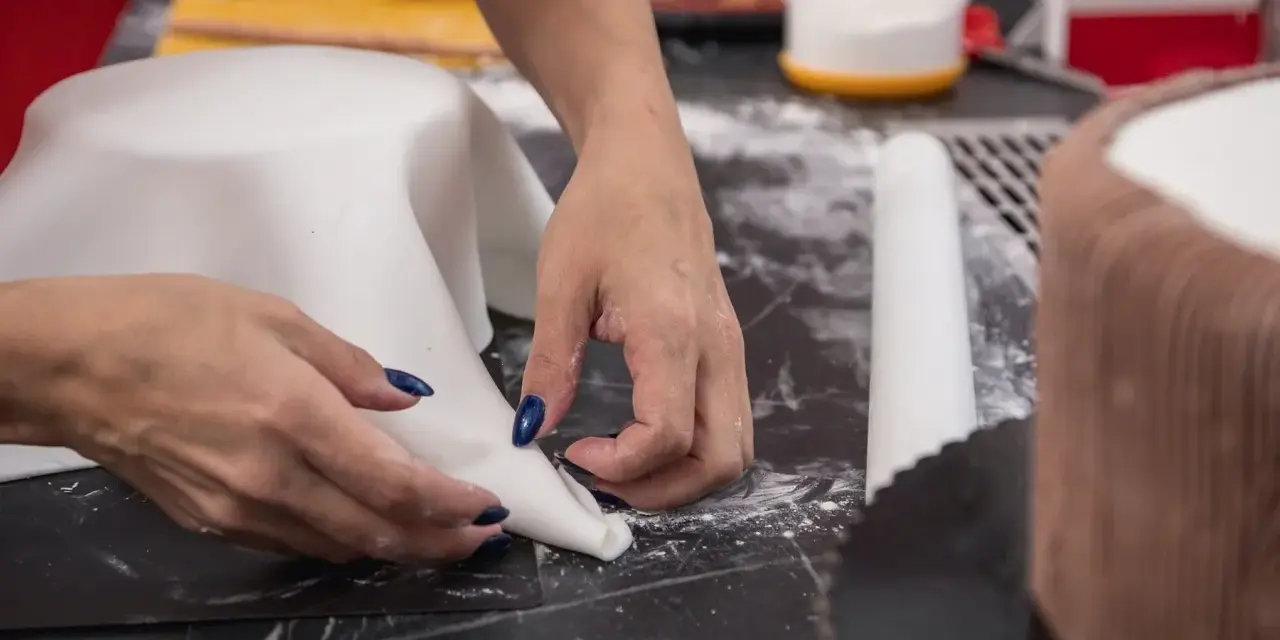 Hände formen weißen Fondant für eine Torte. Hier sind Tipps zum Fondant ausrollen für perfekte Ergebnisse.