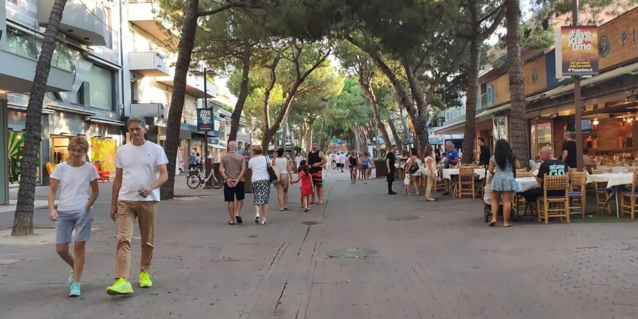 Passeggiata serale nel riccione centro storico, tra negozi e ristoranti all'aperto sotto gli alberi.
