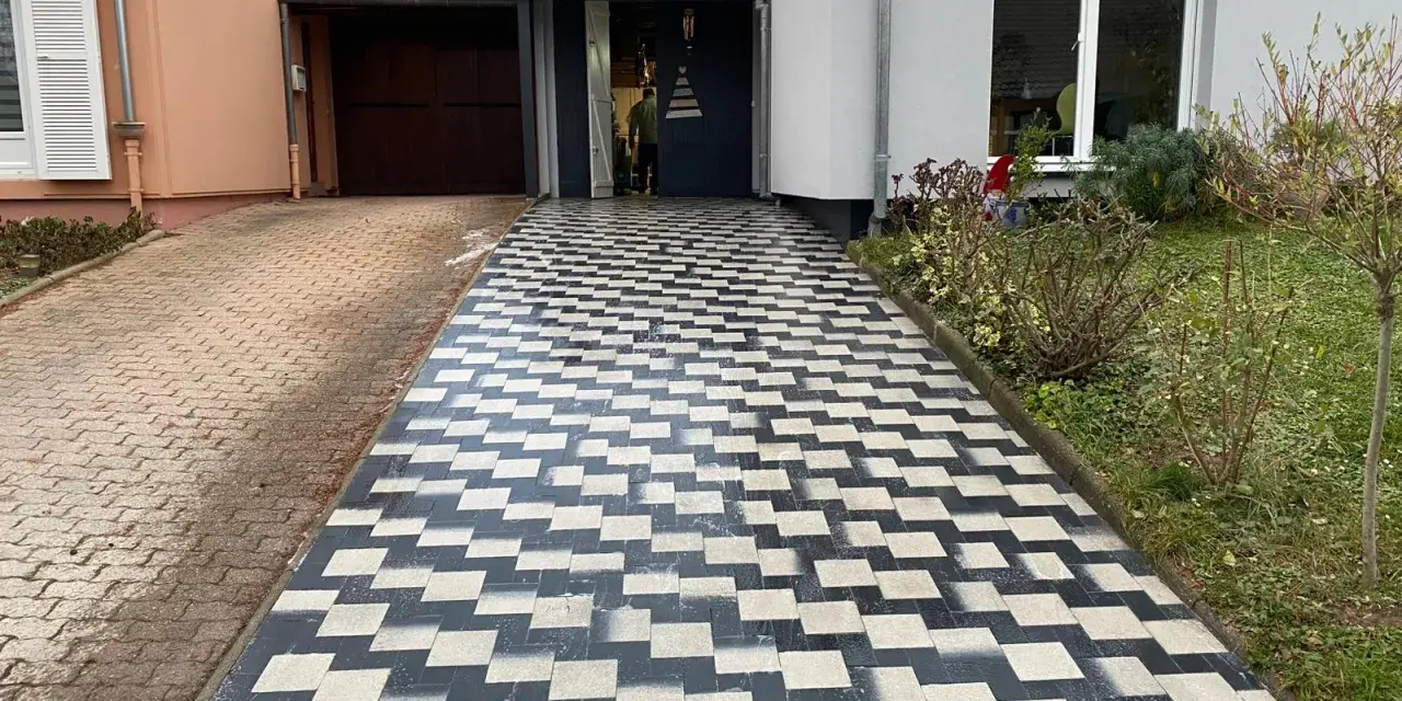 Une allée en pavé au motif géométrique noir et blanc mène à une entrée de garage.