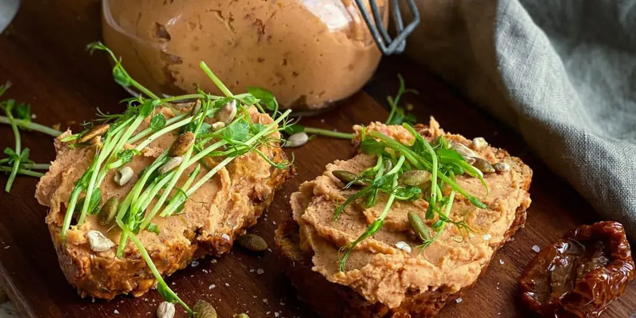 Två rostade brödskivor med krämigt refried beans, toppade med groddar och frön. En burk med pålägget syns i bakgrunden.