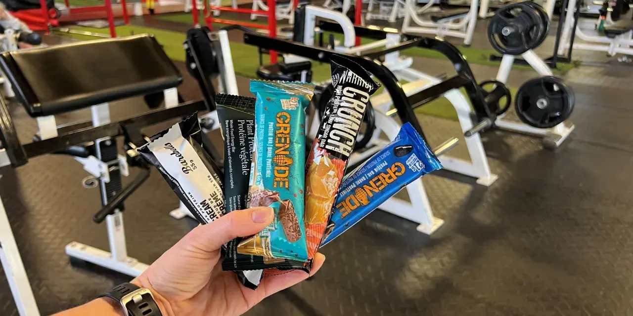 Une main tient plusieurs barres protéinées, parfaites comme collation avant ou après le sport, dans une salle de sport.