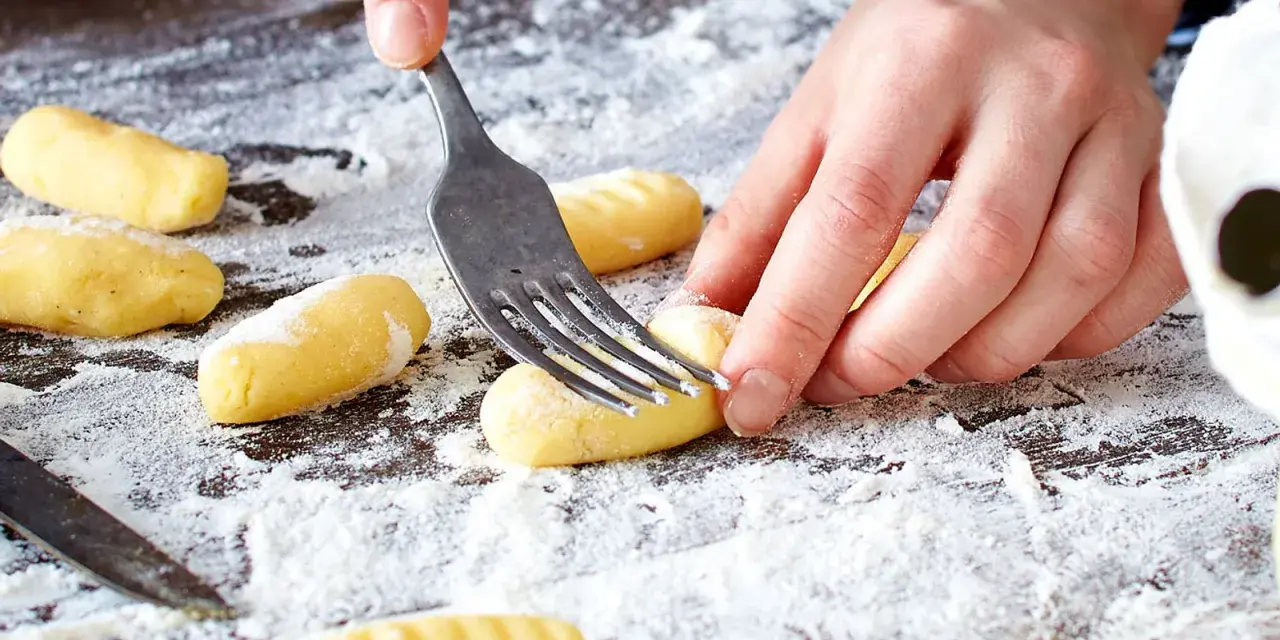 Hände formen mit einer Gabel die Rillen für original Gnocchi auf einer bemehlten Arbeitsfläche.