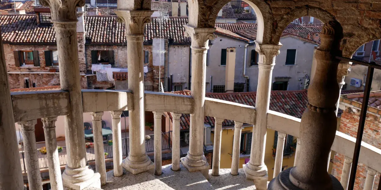 Dalla scala Contarini del Bovolo, vista sui tetti di Venezia. Colonne e archi in pietra creano un gioco d'ombre sulla gradinata.